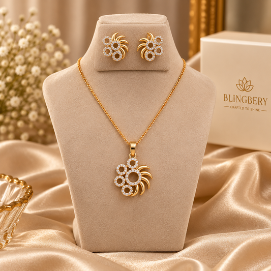 Gold jewelry set displayed on a beige velvet stand, including a necklace with a flower-shaped pendant, matching stud earrings, and a branded Blingbery box in the background.