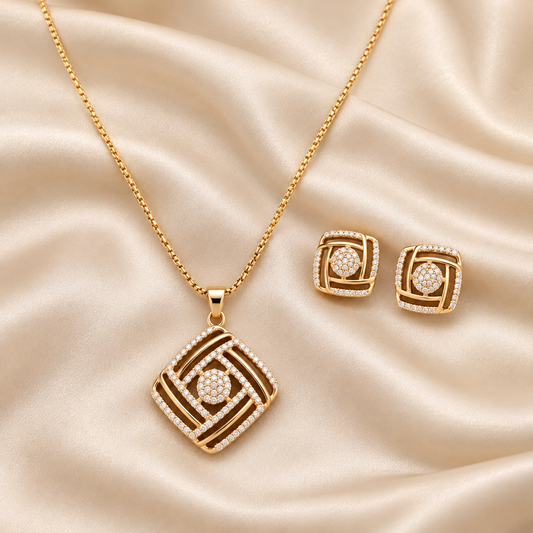 Gold jewelry set featuring a pendant necklace and matching stud earrings with a geometric square design, set against a draped champagne satin background.