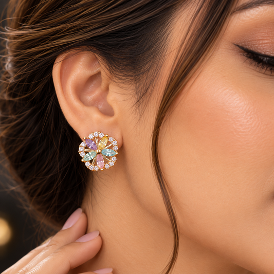 A close-up lifestyle shot of a woman wearing a gold-toned stud earring with a colorful floral design featuring pastel green, pink, yellow, and blue stones.