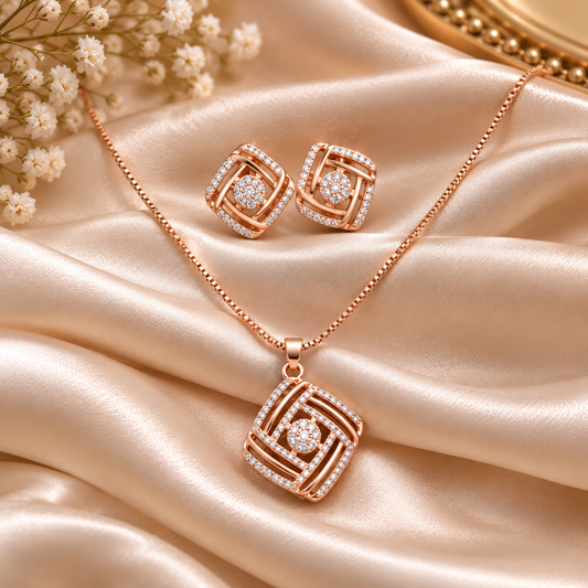 Rose gold jewelry set featuring a necklace and matching earrings with geometric square designs set with clear stones, displayed on draped champagne satin fabric with small white flowers.