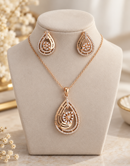 Rose gold jewelry set with a teardrop pendant necklace and matching drop earrings, displayed on a beige jewelry bust. The pendant and earrings feature gold-toned teardrop shapes with clear rhinestone accents and a central floral starburst design.