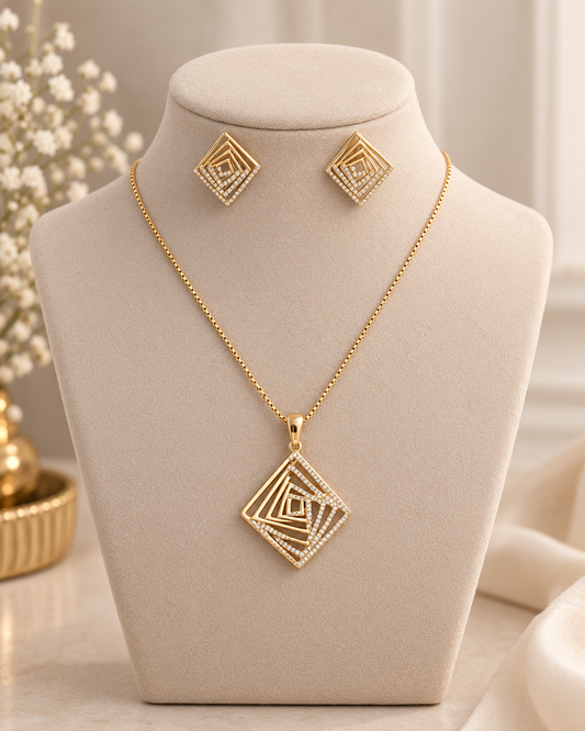 Gold geometric pendant necklace and matching stud earrings displayed on a beige jewelry bust against a soft cream background.