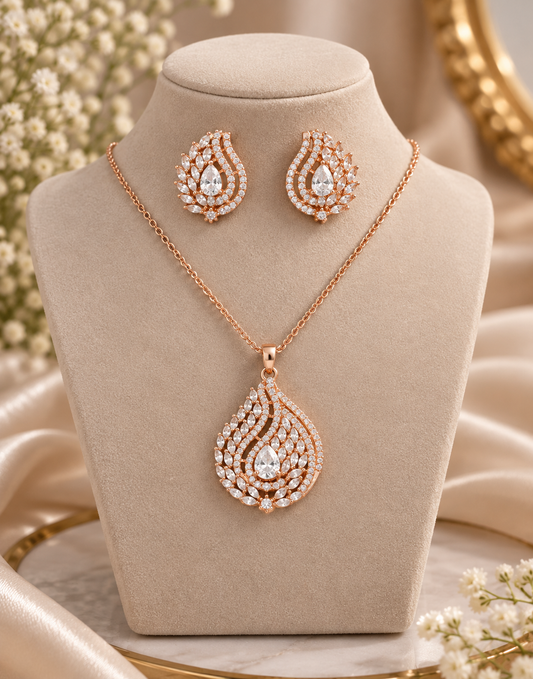 Rose gold jewelry set featuring a teardrop-shaped pendant necklace and matching stud earrings, displayed on a beige jewelry bust with satin and floral accents.
