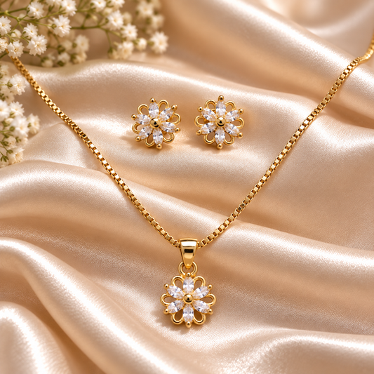 Gold-tone floral pendant necklace and matching stud earrings displayed on draped champagne satin fabric with small white flowers in the corner.
