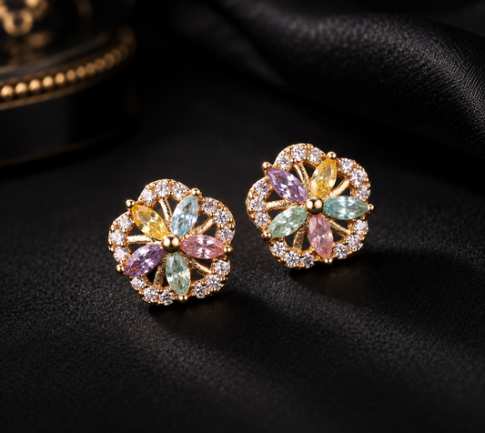 A pair of gold flower-shaped stud earrings with multicolored gemstones and small clear crystals, displayed on a black satin fabric background.
