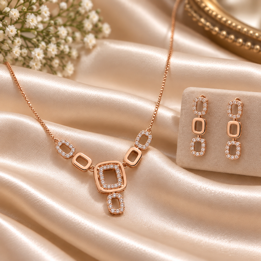 Rose gold jewelry set featuring a necklace and matching earrings with geometric square and oval designs set with clear stones, displayed on champagne satin fabric.